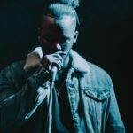 Man Wearing Denim Jacket Singing on Stage